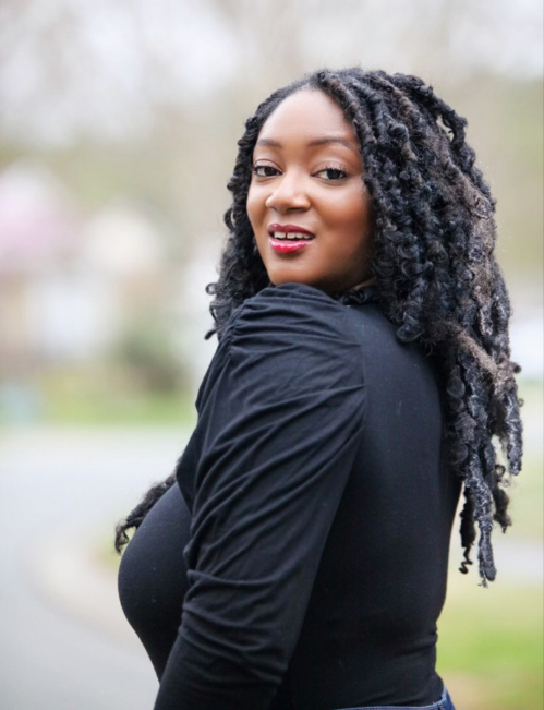 Female team member headshot Female team member with long curly hair wearing a black top, smiling outdoors headshot