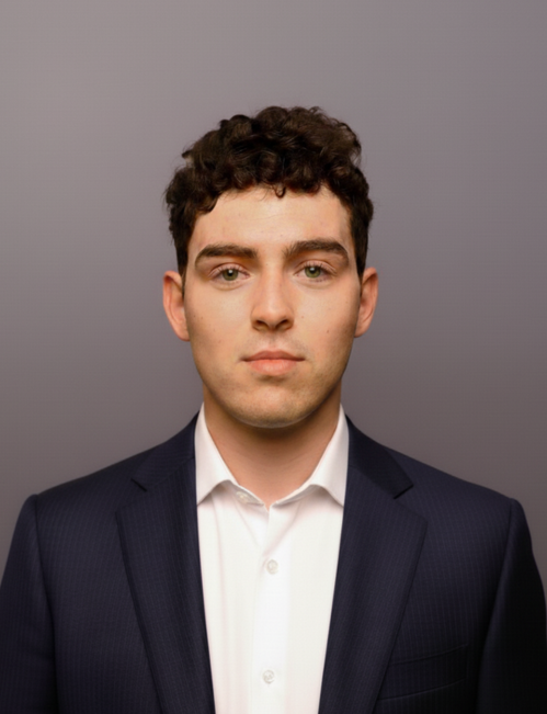 Young male team member headshot Young man with curly hair wearing a dark suit and white shirt headshot