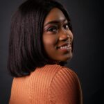 Studio portrait of a beautiful African American woman with a stylish hairstyle, smiling warmly.
