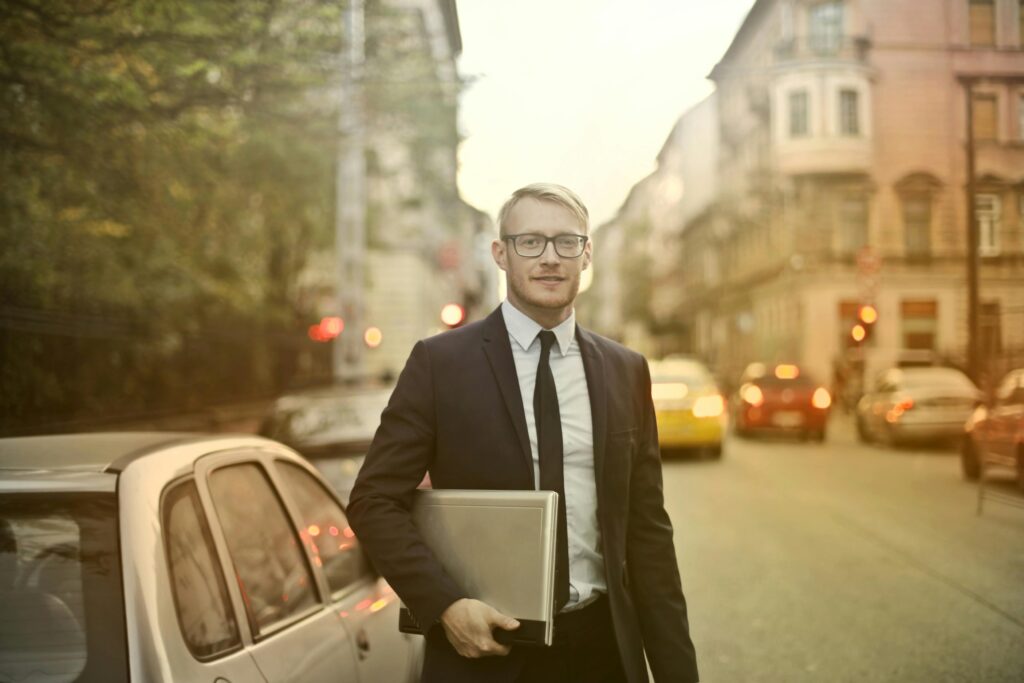 Businessman in a suit holding a laptop on a busy city street with cars