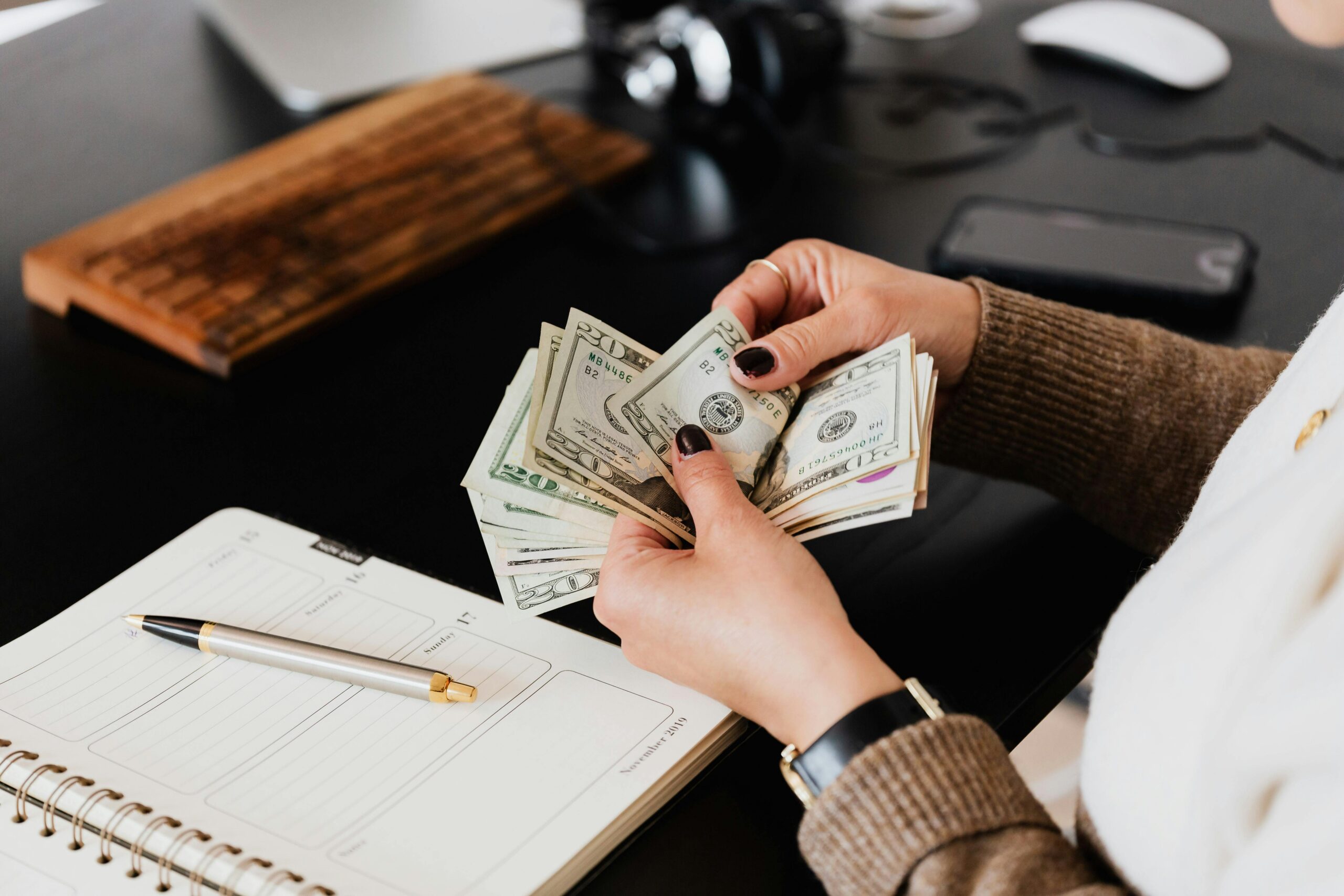 Woman in sweater counting dollar bills at a desk with a notebook